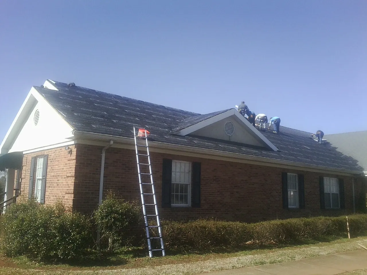 Crew tearing shingles off a brick ranch roof with a ladder set — Metal Roof Repair work by our crew in New Lebanon