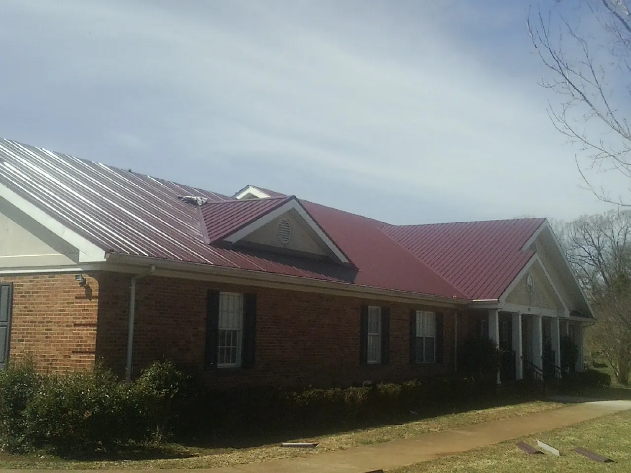 Red metal roof with gabled entries on a long brick building, from a Hail Damage Roof Repair job in New Lebanon