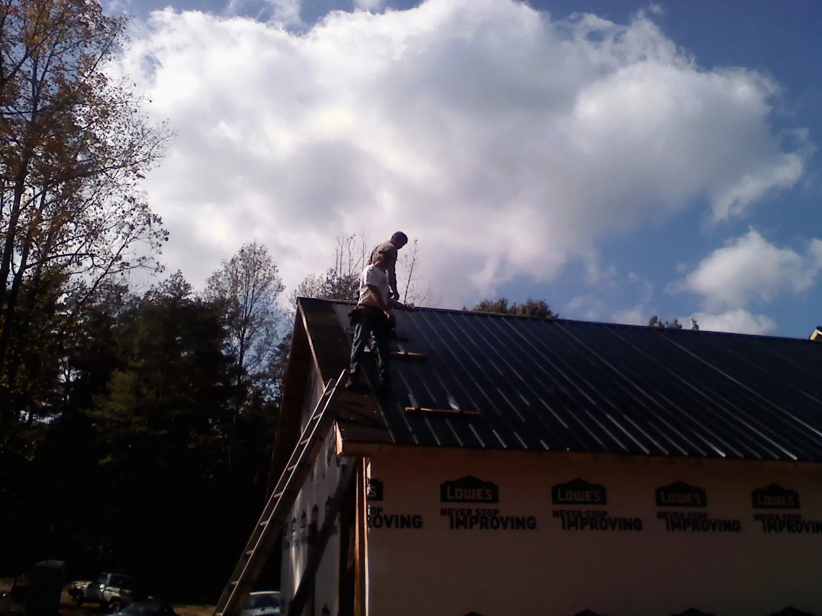 Roofer fastening dark metal panels high against a cloudy sky, from a Roof Inspection job in New Lebanon