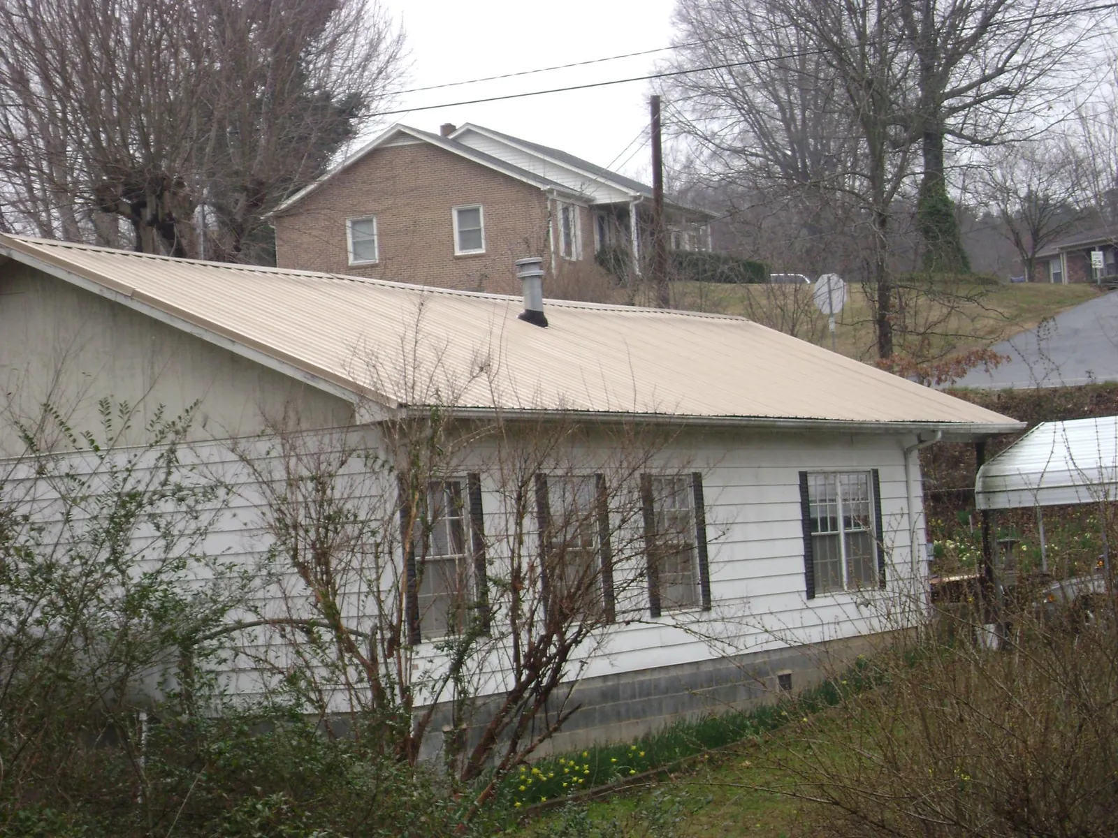Tan metal roof on a white sided house set into a hillside — Commercial Roofing by Roofing Brothers in New Lebanon